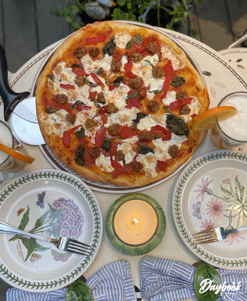 homemade pizza set on an outdoor table with plates and drinks