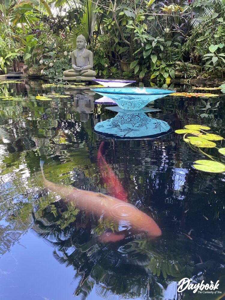 A peaceful koi pond with glass artwork inside a botanical garden.