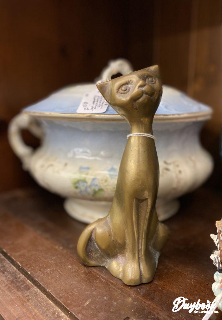brass cat sitting in front of an antique soup Touraine