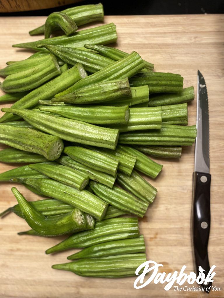 pile of green okra with knife on cutting board
