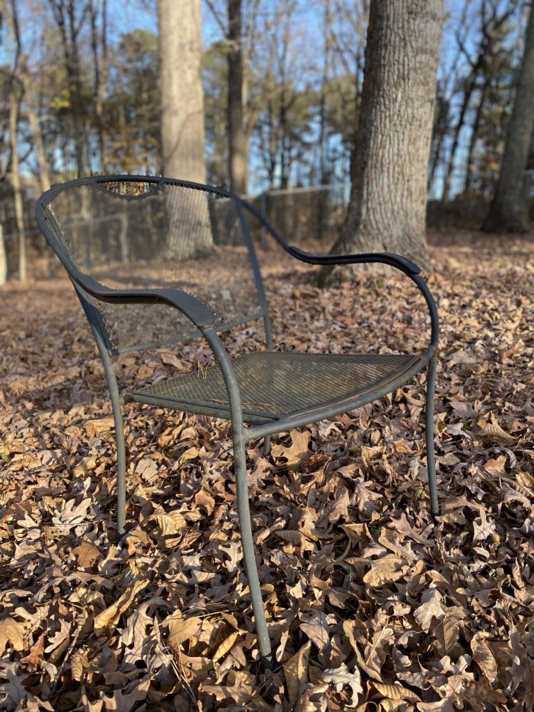 One wrought iron chair sitting in brown leaves in a field