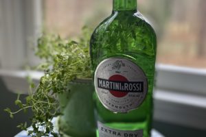 A green bottle of Martini & Rossi Dry Vermouth sitting on a small table in front of a window.