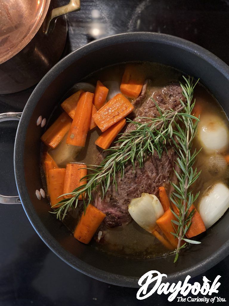 Beef pot roast in a deep pan with carrots and rosemary