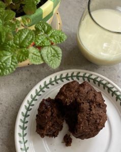 Triple chocolate banana muffin on a plate next to a glass of milk and a green plant
