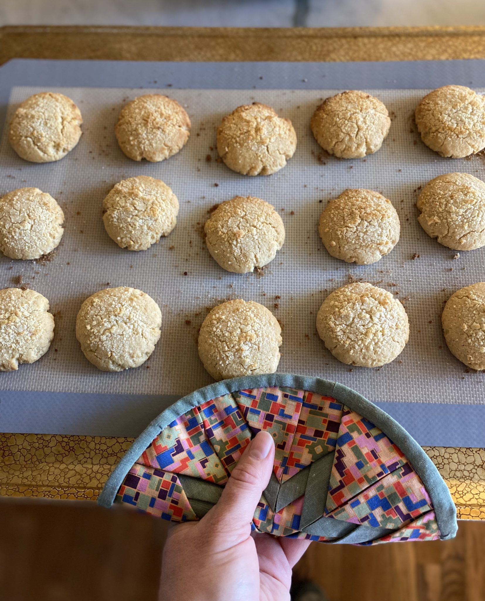 A cookie tray of cooked apple crumble cookies held with a colorful pot holder.