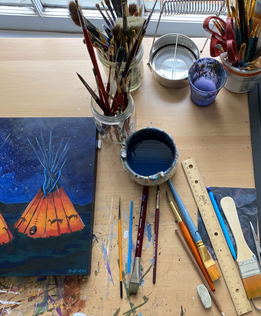 An artist's table with her supplies out and a painting on the left
