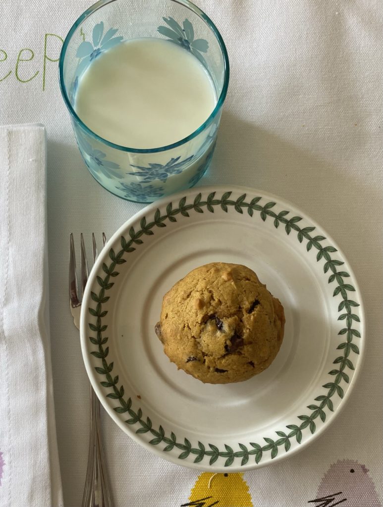 A pumpkin muffin on a small plate with a glass of milk beside it