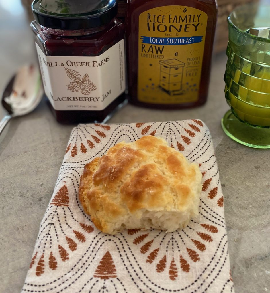 A homemade biscuit on a cloth napkin next to honey and jam.