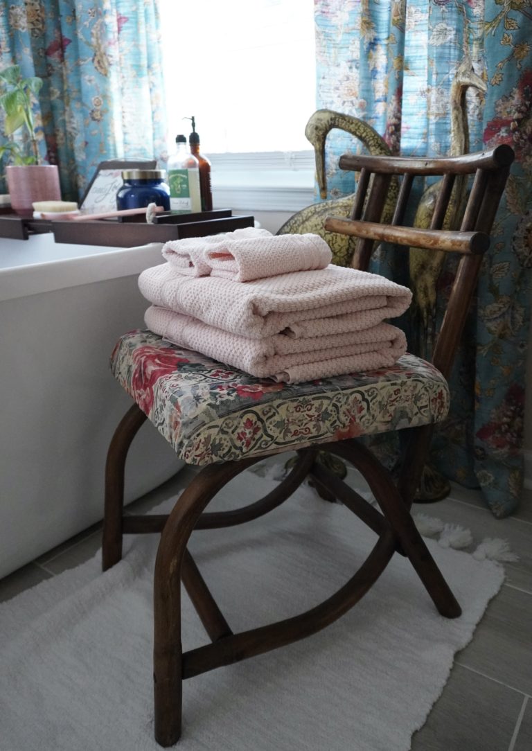 Wooden rattan chair with pink towels stacked next to a white bathtub