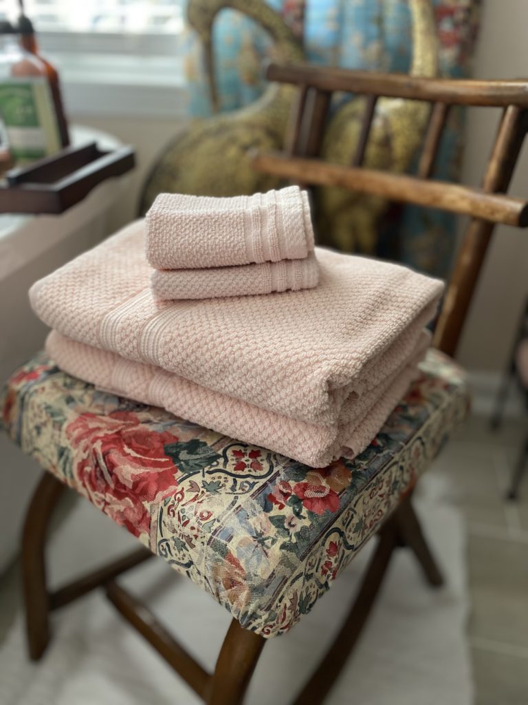A rattan chair with a floral seat and folded pink towels on top.