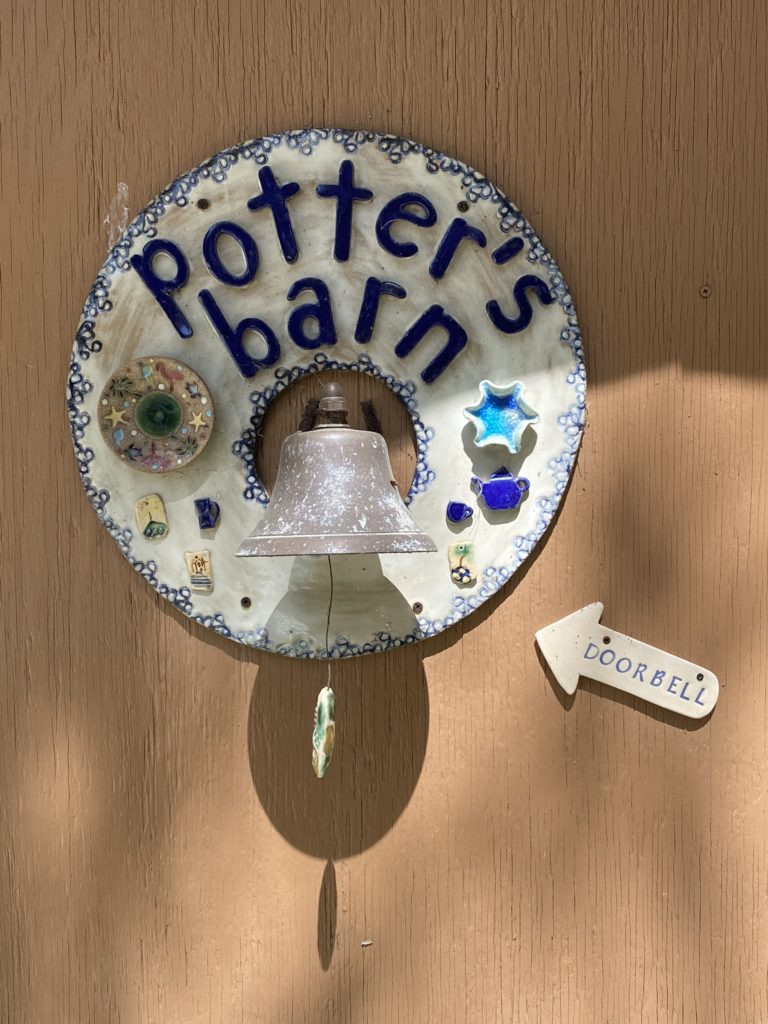 A handmade pottery sign that reads The Potter's Barn with a doorbell in the middle.