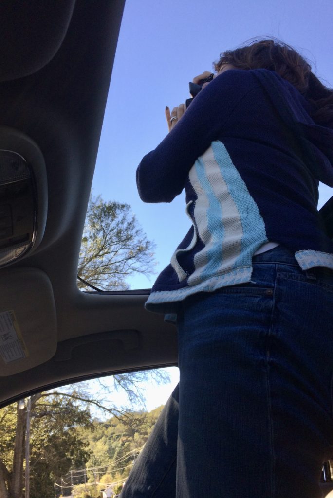 Kristy standing up in her car to photograph a local church through the sunroof.