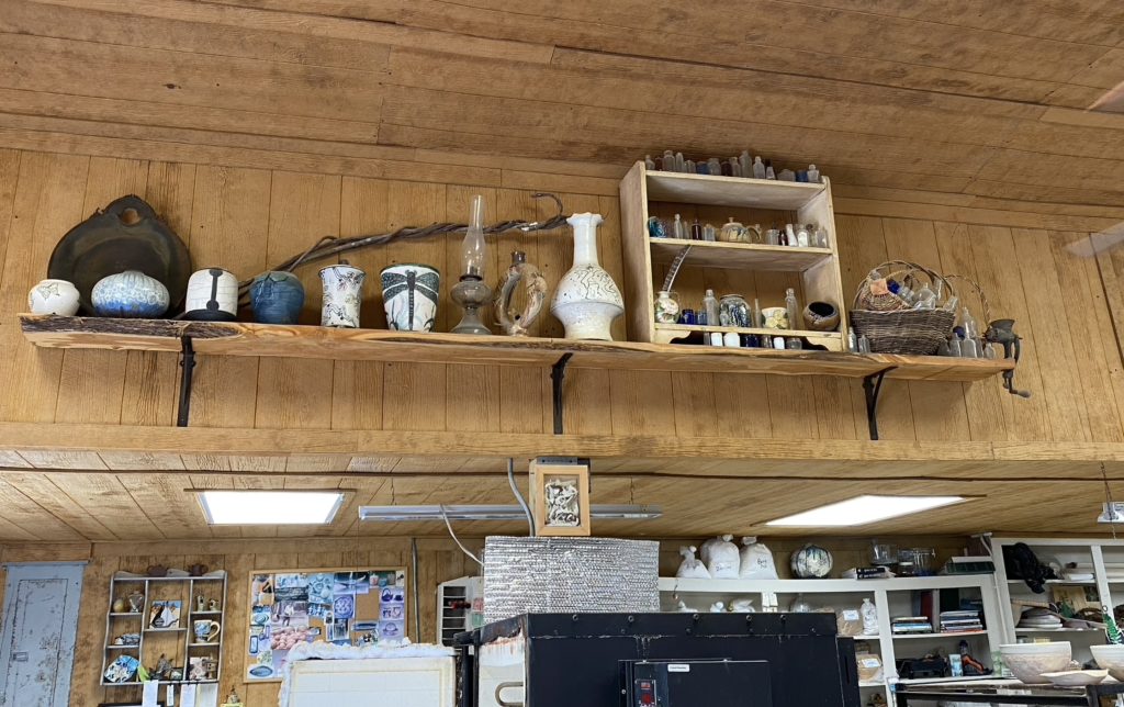 A collection of pottery and glass jars on a high shelf in a potter's barn.
