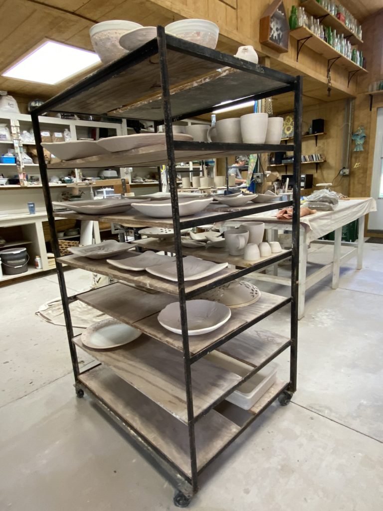 A tall metal shelf with pottery ready to be glazed.