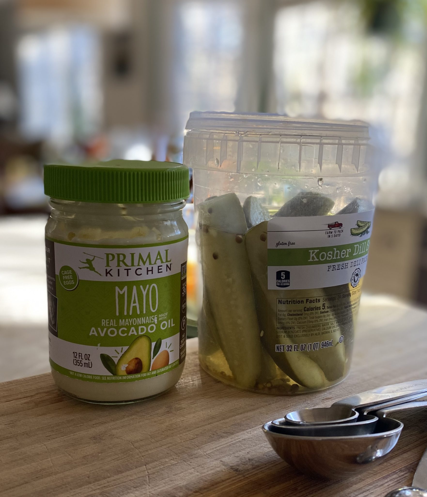 A jar of Primal Kitchen mayonnaise and a jar of dill pickles on a kitchen countertop.