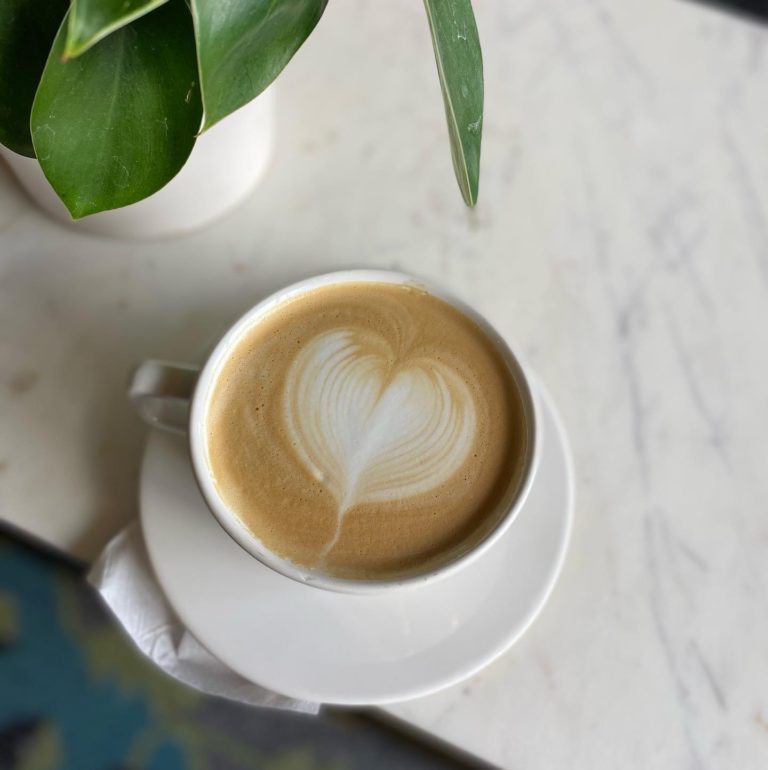 A latte in a white coffee cup with a heart design in the cream.