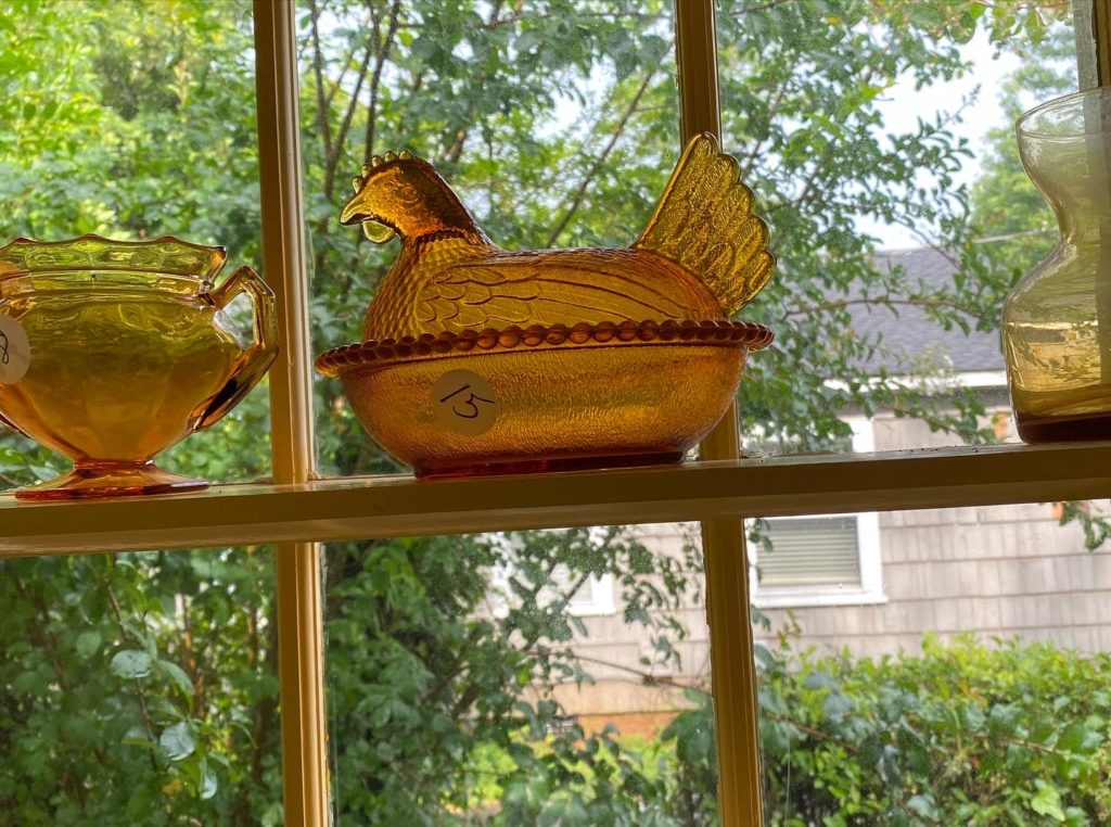 An amber glass chicken dish in a sunny yellow window of an estate sale