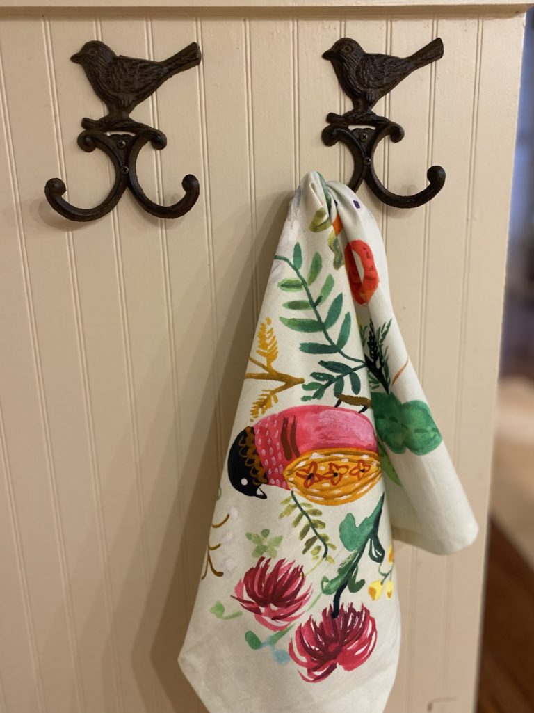 A colorful kitchen towel hanging on an island with two metal hooks.