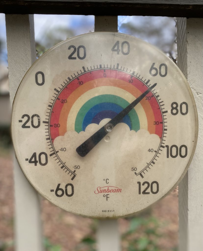 A round vintage thermometer with a rainbow in the background.