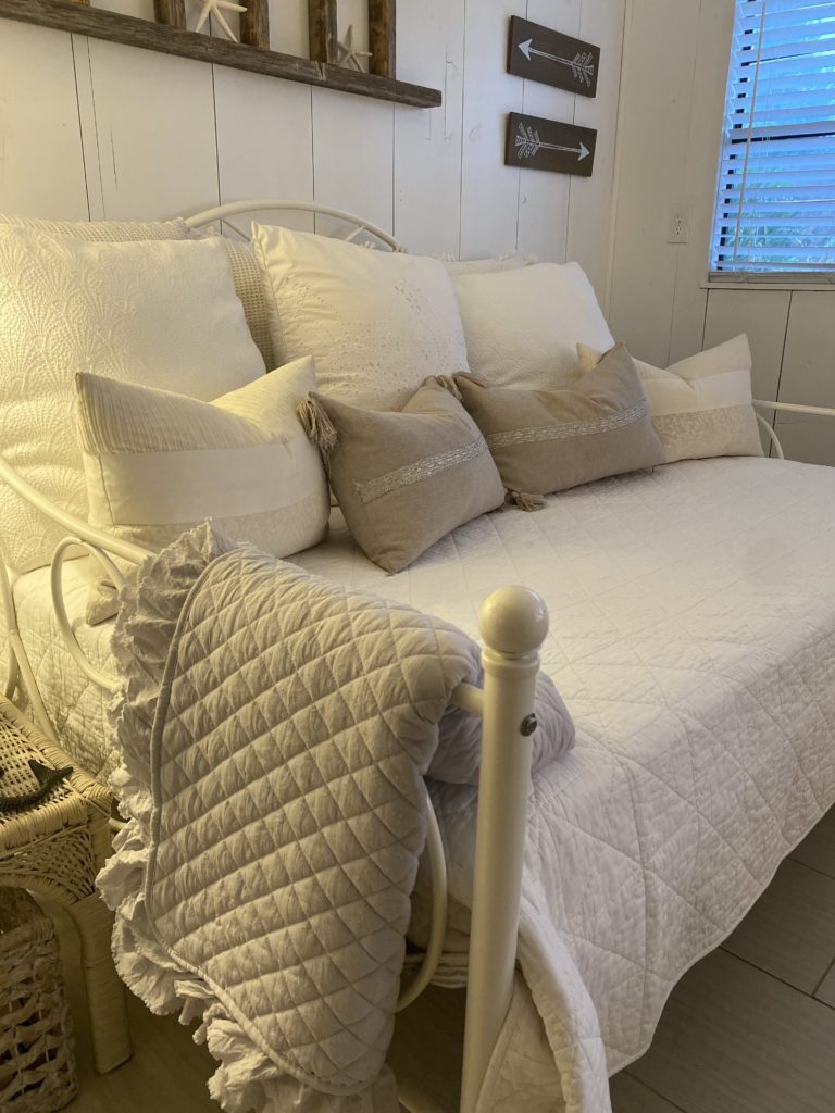 The side view of a daybed with a white coverlet and white throw pillows.