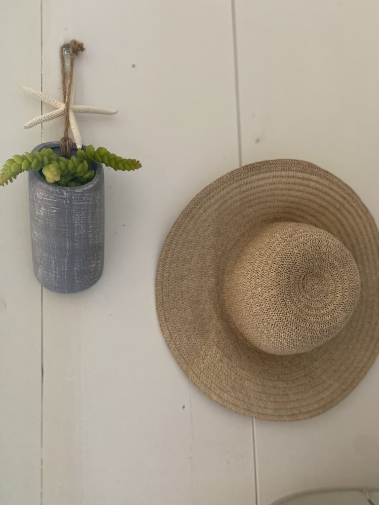 A pottery plant holder and a straw hat hanging on a white wall inside a Florida cottage.