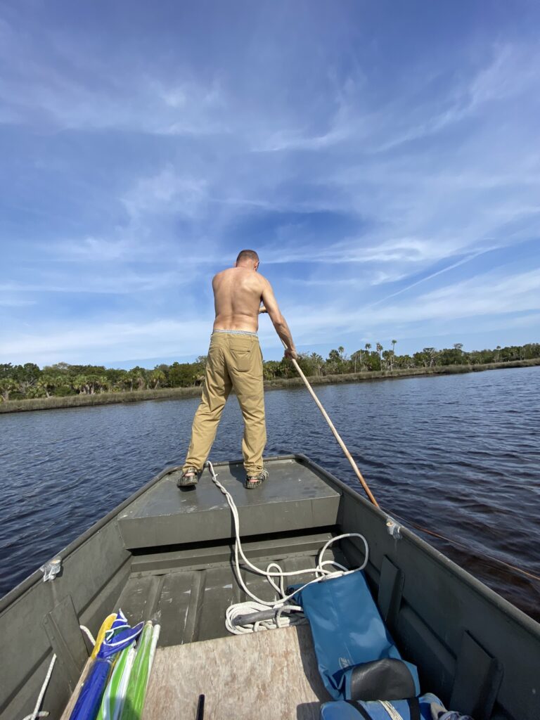 John standing on the bow of the boat navigating through the shallow river