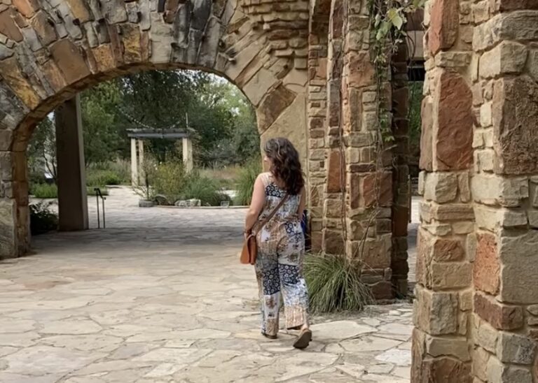 Lady walking through a stone archway at the Lady Bird Botanical Garden