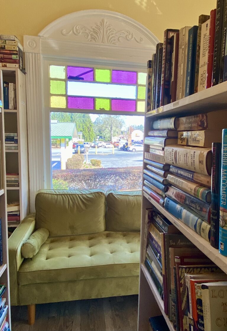 A view from inside a bookstore looking at a green velvet sofa with a stained glass window above.