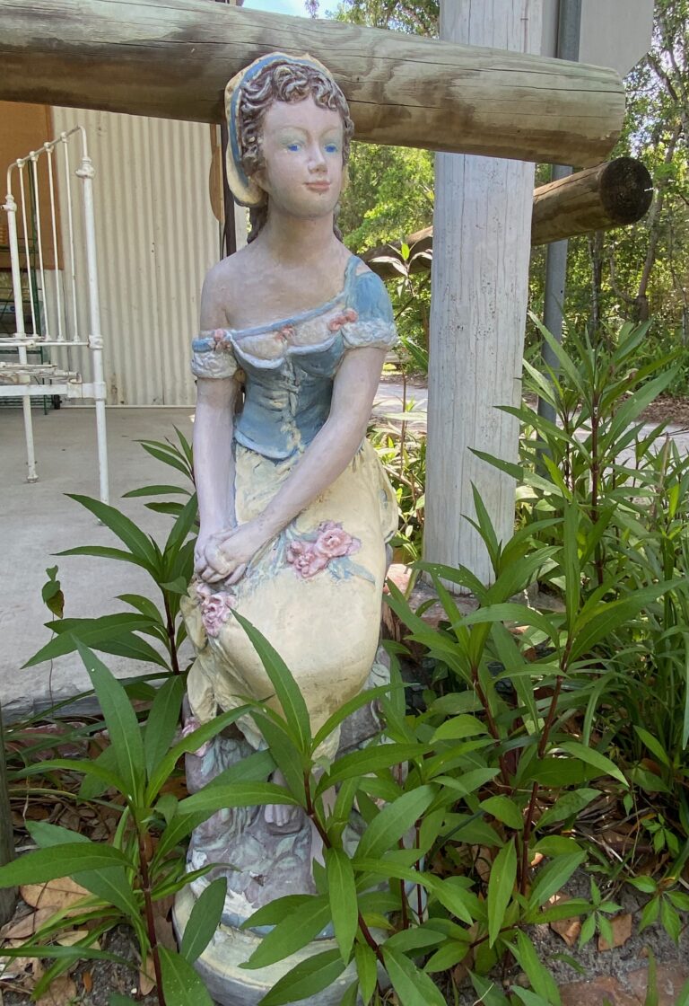 A white and blue concrete statue of a lady in a dress with one shoulder sleeve falling off