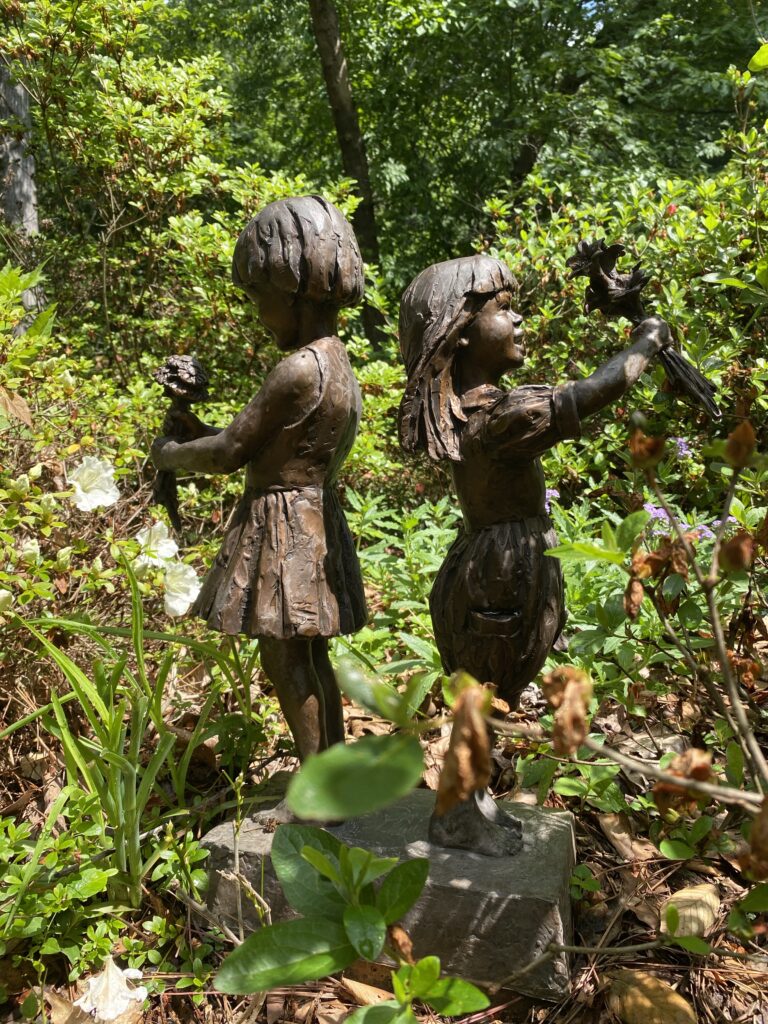 Two bronze statues of young girls in a flower garden at the University of Georgia