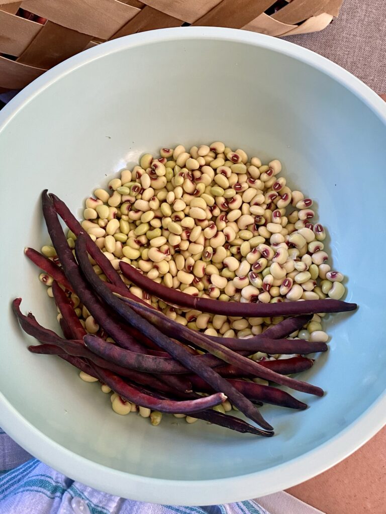 A green bowl with shelled purple hull peas and a few unshelled peas on the left.