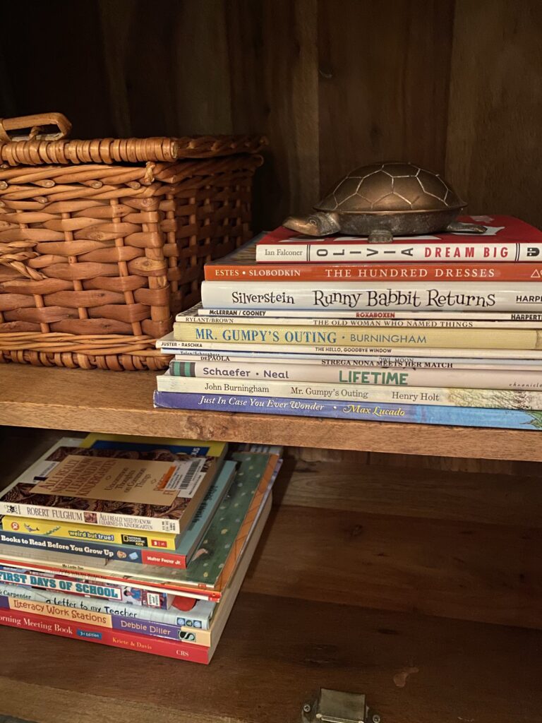Two stacks of books on a small bookshelf with a wicker basket to the left.