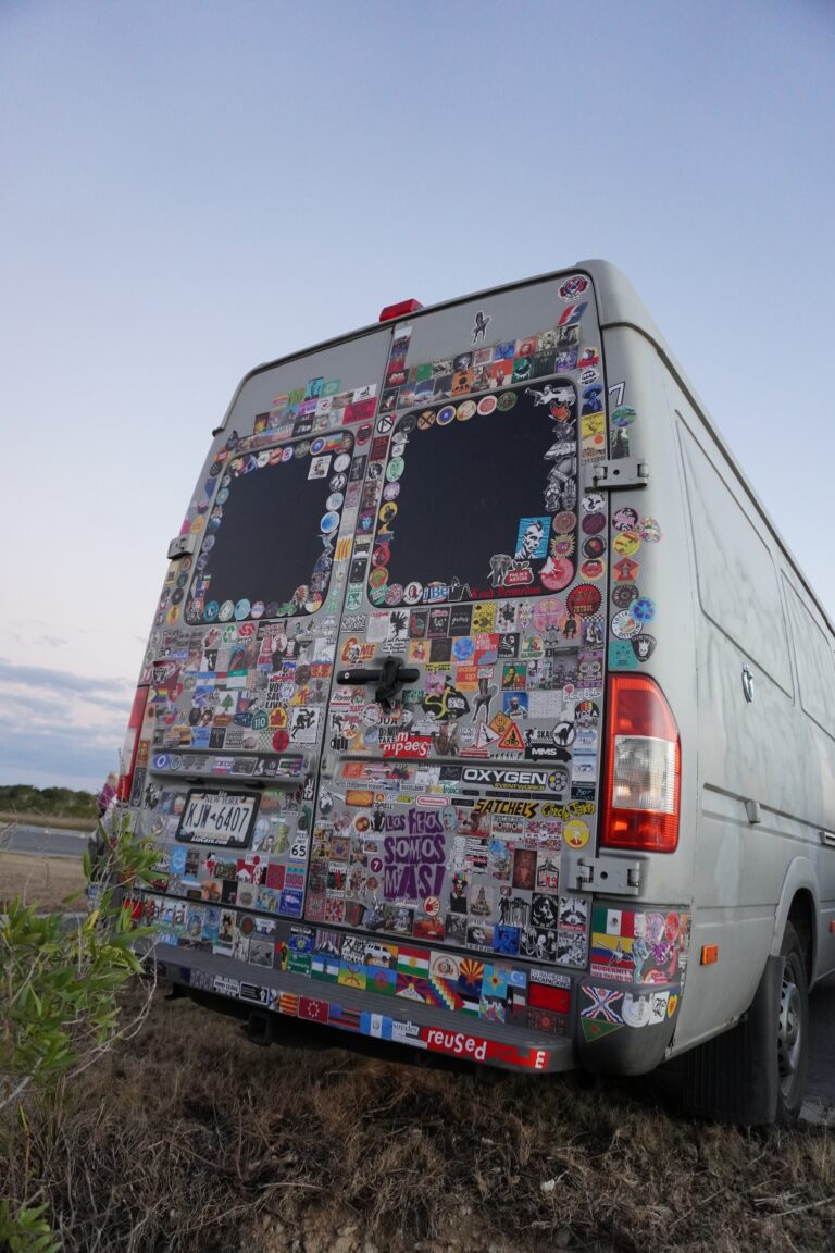 The back of a white van covered in bumper stickers and parked by the river in Florida