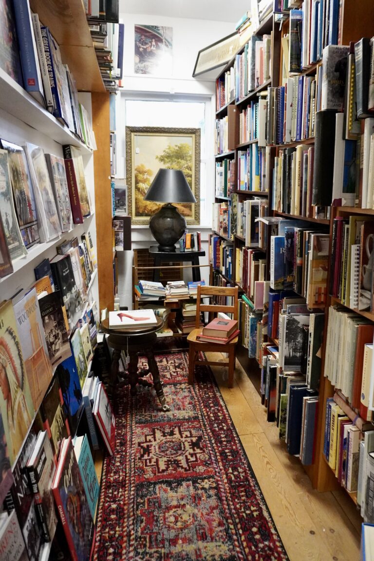 Inside a bookstore along a narrow row of books with chairs on either side.