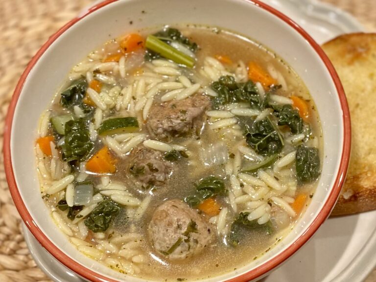 A bowl of Italian Wedding Soup in a white and orange bowl